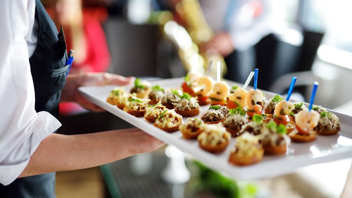 A waiter holds a white plate of canapés